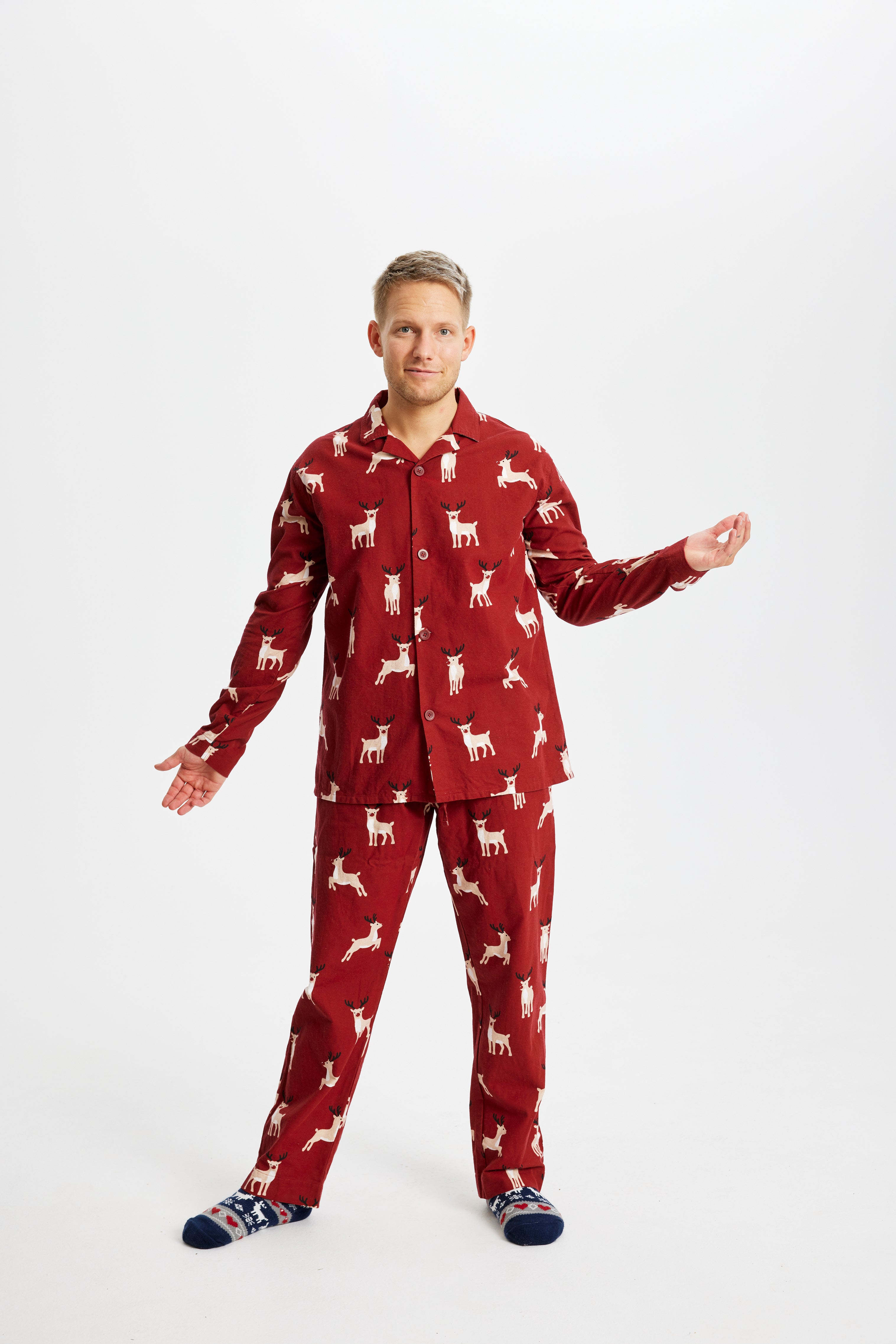 Een poserende man in een rode kerstpyjama met rendieren erop.